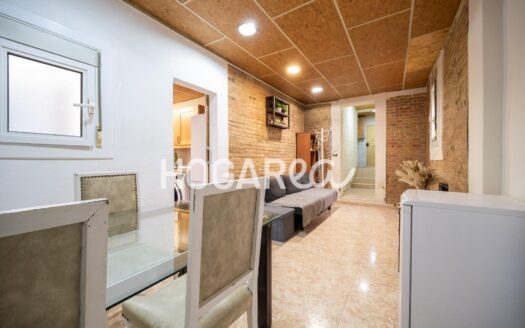 Este bajo de 74 m² en calle Vallespir ofrece un acogedor salón con paredes de obra vista, amplia cocina con acceso mediante escaleras metálicas a una terraza interior, dos dormitorios y baño con d
